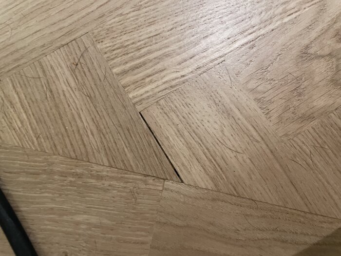 Fiskbensparkett med en glipa mellan stavarna och ojämnt slipad yta. En trasig bit och bristande passform vid kanterna syns.