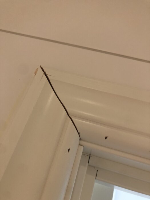 Spricka i vit dörrkarm med märken på ytan i en inomhusmiljö.