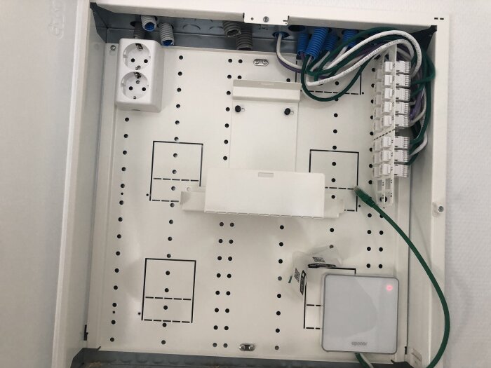 Elcentral med eluttag, ordnade kablar och patchpanel i ett vitmonterat skåp.
