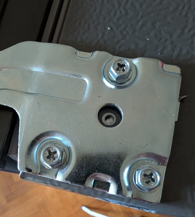 En metallbeslag med fyra skruvar monterade, två med Philips eller liknande skruvhuvud, på en yta av ett möbel- eller byggprojekt.