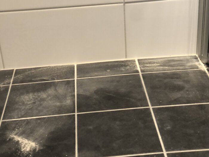 Svart och vit kakelvägg med svart klinkergolv där det syns spår av fogmassa på golvytan, troligen under ett renoveringsarbete i ett badrum.