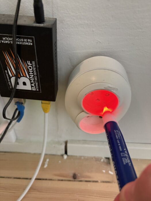 Person testar elektriskt uttag med spänningspenna, ljus indikerar ström i övre uttag, kablar och nätverksenhet synliga bredvid.