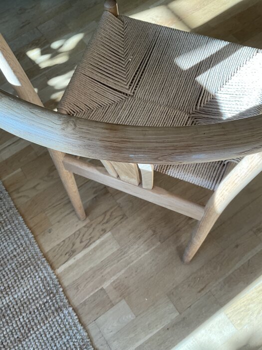 Trästol med rundad rygg och flätat sitsmönster i ljus träfärg, placerad på ett parkettgolv.