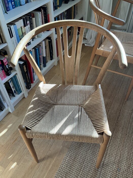 Trästol med ljusbrun flätad sits och böjd ryggstöd i en lägenhet med bokhyllor i bakgrunden.
