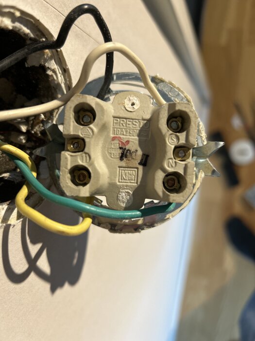 Äldre strömbrytare med fem kablar i olika färger, inklusive svart, vit, gul och grön, anslutna till terminaler på vägg.