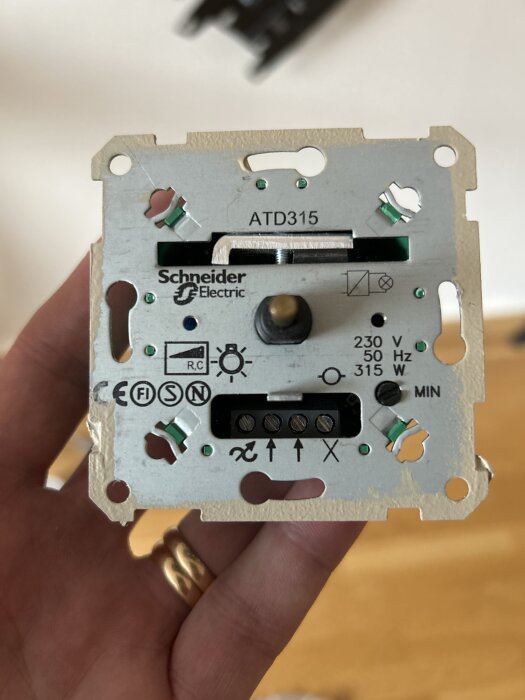 Gammal strömbrytare med "Schneider Electric" logga och anslutningssymboler, hålls i en hand.