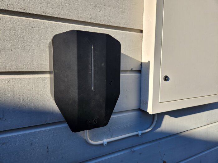 Laddbox monterad på en vägg utomhus, med vit kabel som ansluter till en elcentral.