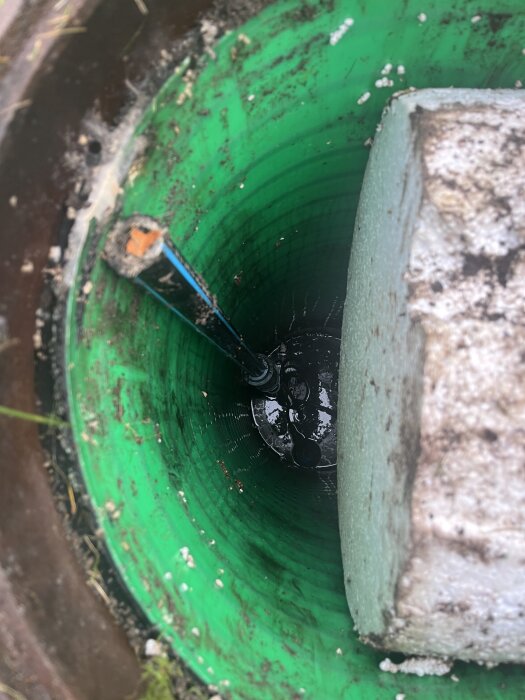 Grön cylindrisk behållare nedgrävd cirka två meter, med en pumpventil synlig i botten, delvis täckt av jord och vit isolering på kanten.