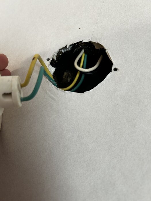 Elektriskt takuttag med synliga färgade kablar bakom ett runt hål i väggen.