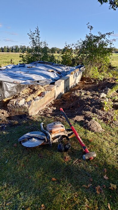 Rivning av betongfundament med plan för sänkning. Bilden visar en kapmaskin, slägga och skyddsutrustning vid sidan av en täckt konstruktion.
