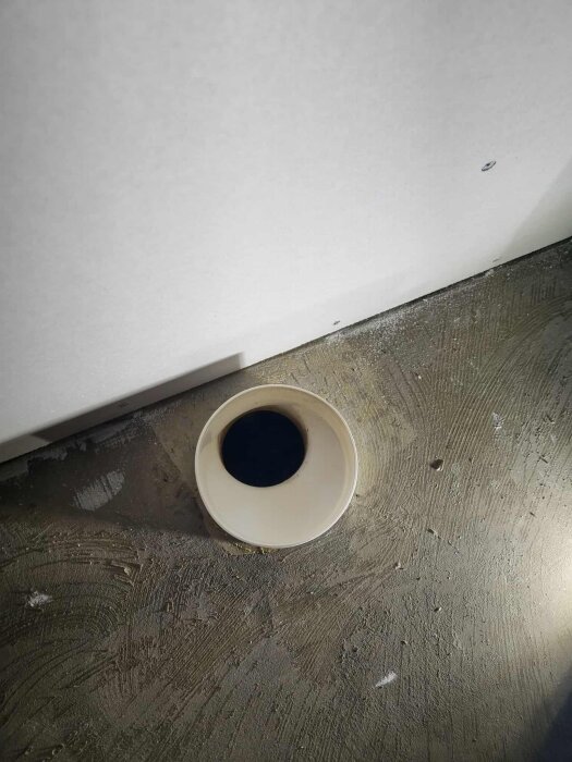 Rör i golvet avsett för toalettanslutning, sett uppifrån. Gjuten cementgolv omger röret.