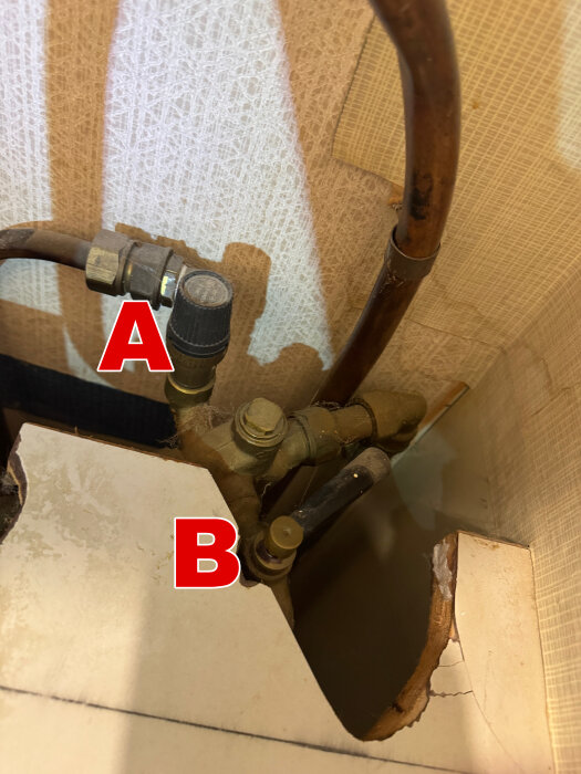 Vattenberedare från 70-talet med två kranar, märkt "A" och "B", monterade i ett trångt utrymme med kopparrör.