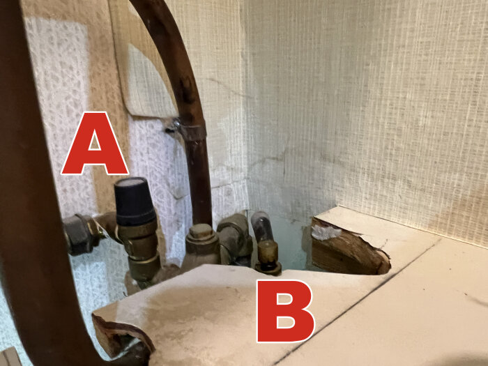 Kopparrör och två märkta kranar, "A" och "B", kopplade till en äldre varmvattenberedare.