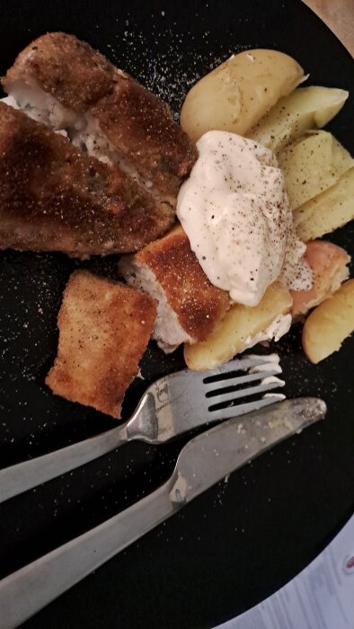 Panerad gös och egna potatisar på en tallrik med majonnäs, två köksredskap ligger bredvid.