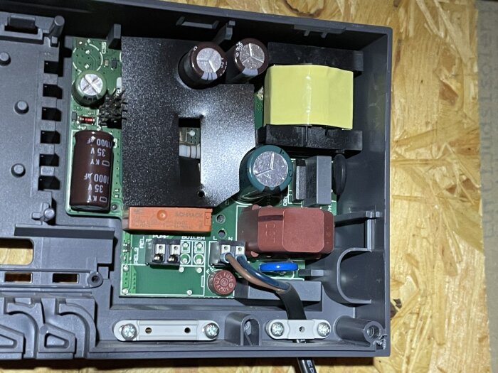 En närbild av insidan av en elektronisk enhet med kretskort, kondensatorer och andra komponenter, placerad i ett grått plasthölje.