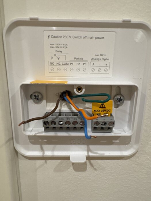 Anslutning av kablar i en termostat, med bruna, blå och orangea kablar kopplade till respektive anslutning. Grön kabel ej ansluten.