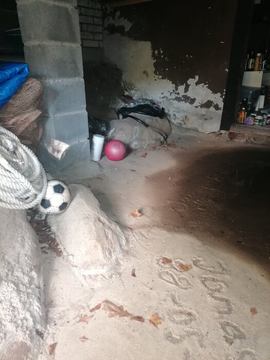 Vattenskada i källare med fuktiga väggar, fotboll, rep och andra tillhörigheter på golvet. Väggarna visar tecken på avflagning av färg.