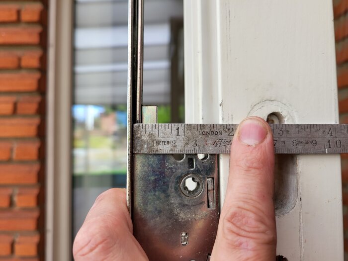 Närbild på en mätsticka som mäter dornavståndet på en spanjolett i en dörrkarm.