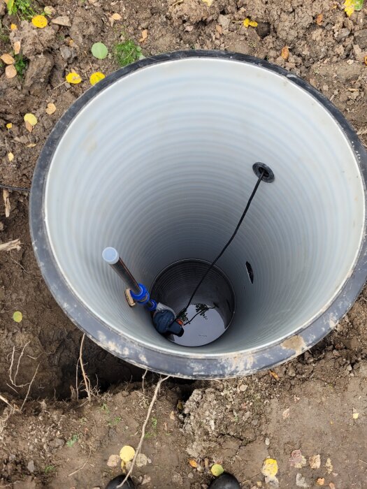 Glidkoppling i botten av en pumpbrunn, med intilliggande rör och kabel, synlig ovanifrån med jord runt omkring.