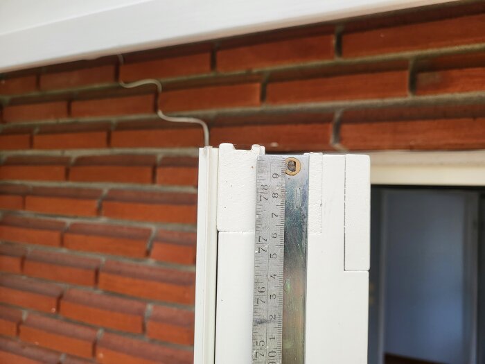 Mätning av dörrkarm med metalllinjal mot tegelvägg i bakgrunden, för att bestämma dornavstånd för ny spanjolett.