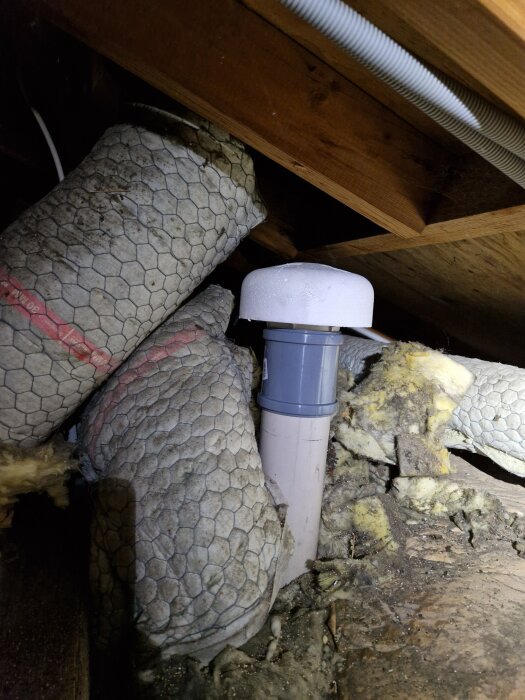 Tryckutjämnare installerad på vinden, omgiven av isoleringsmaterial och synliga takbjälkar.