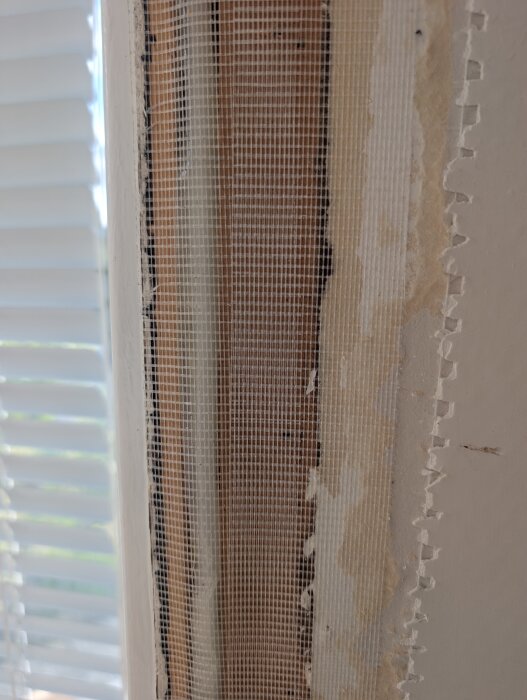Fönsterram utan foder med synligt nät och springa, redo för spackling och renovering.