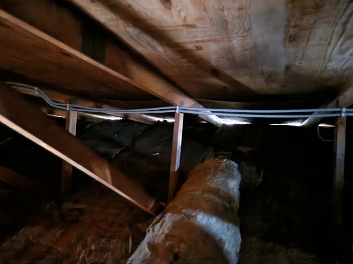 Vindutrymme med synliga takstolar och plywood, ventilation i takfoten, samt isolering och eldragning syns.