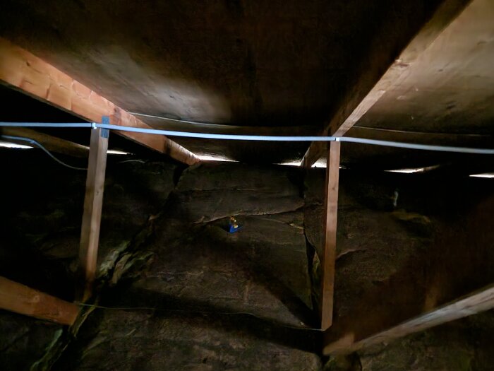 Loftutrymme med plywoodtak som hänger mellan takstolarna, synliga träbjälkar och isolering.