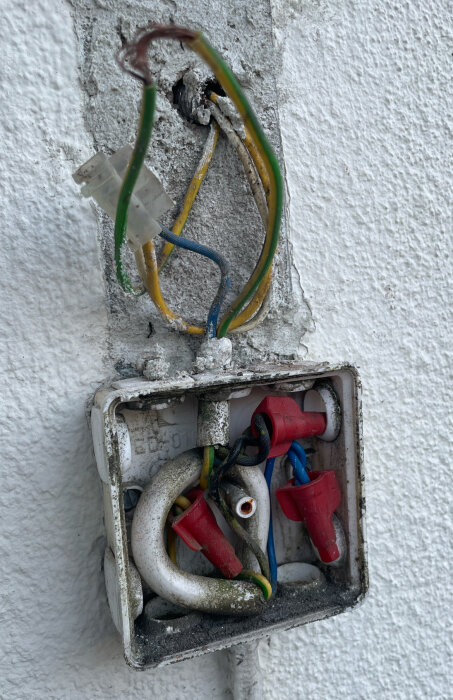 Gammalt elinstallationsskåp med olika färgade kablar (blå, gul, grön, svart) och röda kopplingar. Skåpet är slitet och smutsigt.
