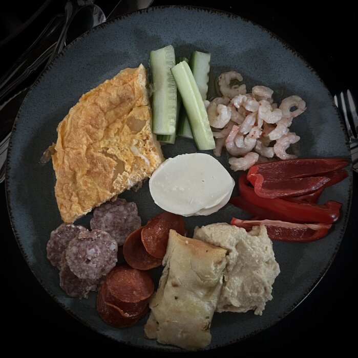 Tallrik med tapas: tortilla, gurka, chilifrästa räkor, paprika, mozzarella, korv, salami, pinsa och hummus.