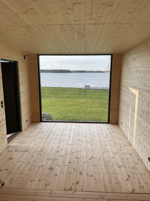 Rum med träpanel och stort fönster med utsikt mot en sjö, nyligen färdigställd för en bastu och relaxavdelning.