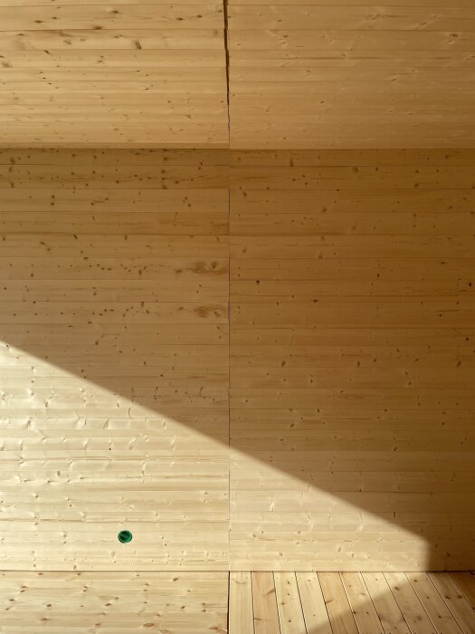 Vägg med nyligen monterad träpanel med ljus- och skuggspel, synlig skarv förberedd för glasvägg mellan bastu och relax.