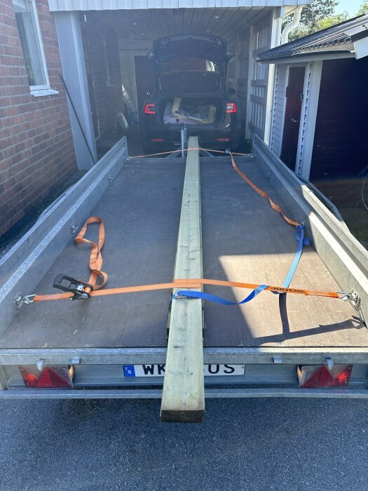 Släpvagn med bräda fastsurrad med spännband.