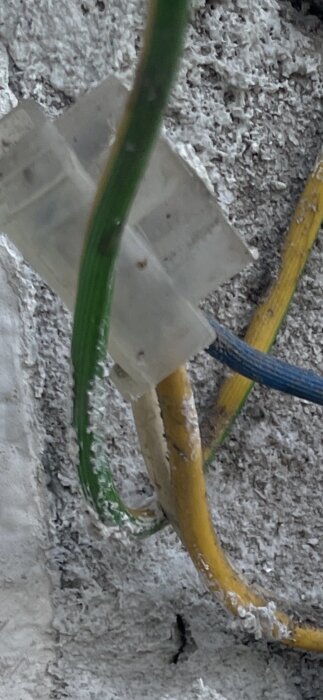 Färgglada elkablar i en kopplingsbox mot en vägg med vit puts.