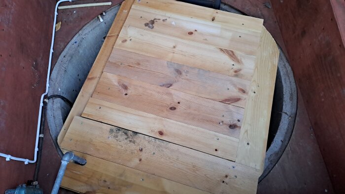 Trälock byggt av golvbrädor täcker en pumpbrunn, del av ett projekt för att förbättra temperaturisolering inför vintern.