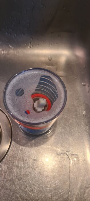 Ventil i ett glas med varmt vatten och diskmedel i ett handfat, omgiven av lödder.