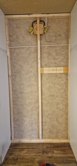 Vägg med trästöd och elledningar synlig efter borttagen spånskiva, del av renoveringsprojekt.