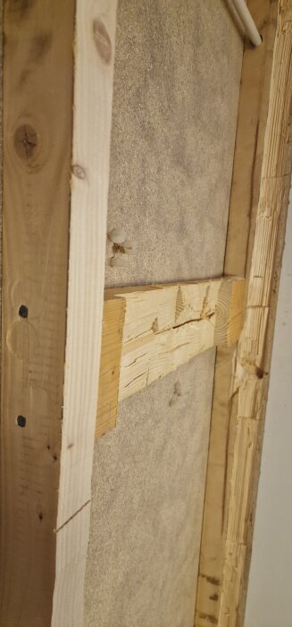 Närbild på en träkonstruktion där en spånskiva har tagits bort, med träbalkar och sågspån synliga.