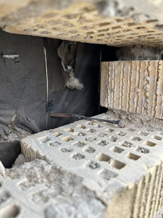 Närbild av sliten skalmur med gamla kramlor från 1957, synliga mellan solida och perforerade murstenar.