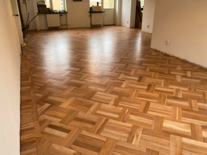 Träparkett golv i ett rum med vita väggar och fönster som släpper in naturligt ljus.