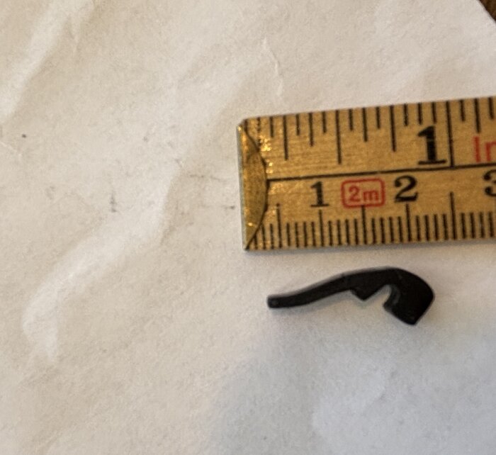 Svart tröskeltätningslist från 80-talet jämte trälinjal med millimeterangivelser, placerad på vit bakgrund.