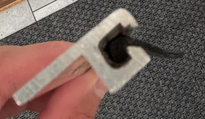 Närbild på en sliten gummitröskeltätlist, hålls i handen, mot bakgrund av en mönstrad matta.