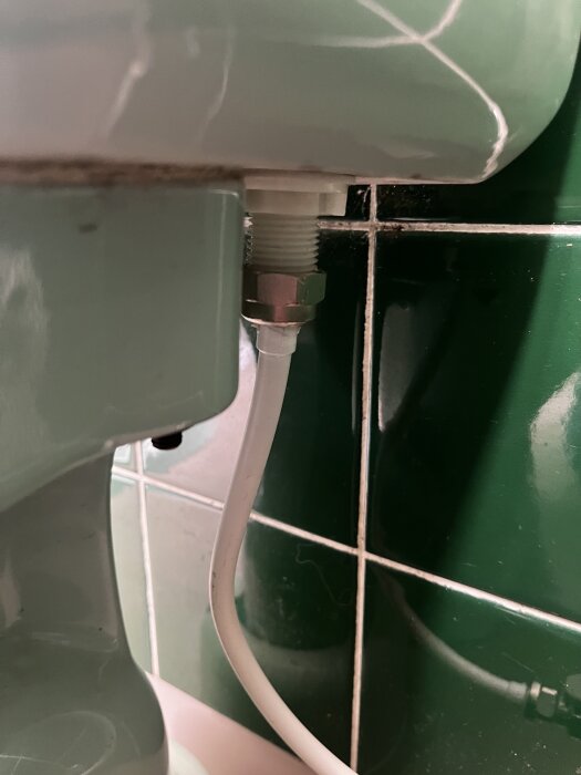 Närbild på en VVS-koppling med en vit slang ansluten under en grön cistern i ett badrum.