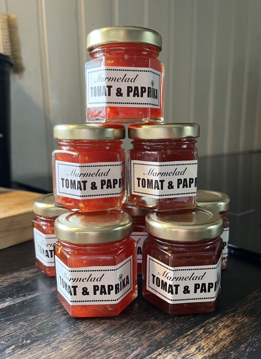 Små glasburkar med tomat- och paprikamarmelad staplade i en pyramid, klara att ges bort som julklappar.