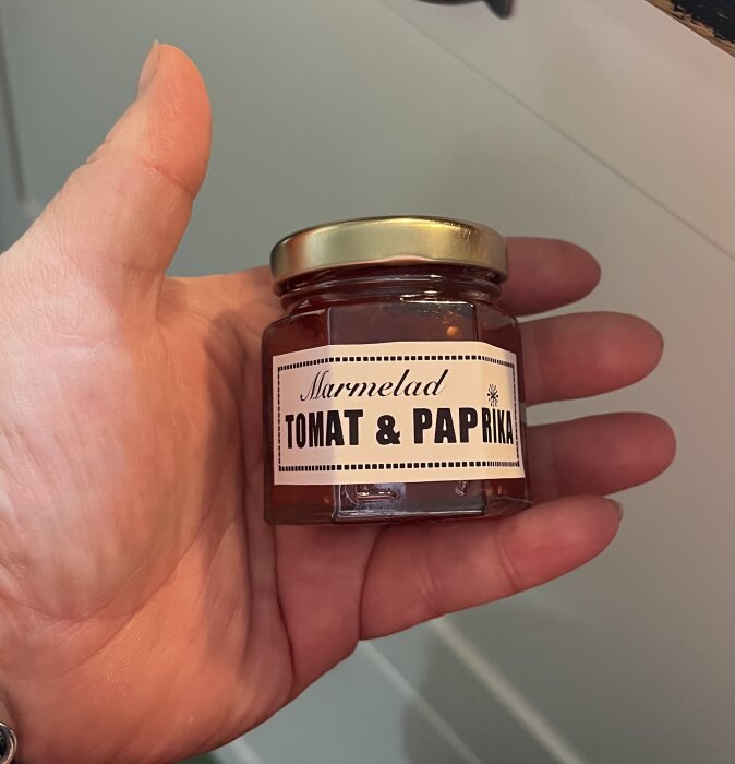 Hand håller en liten burk med etiketten "Marmelad Tomat & Paprika", en hemlagad julklapp.