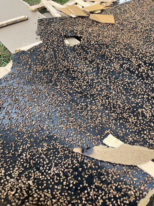 Underlag av svart material med bruna korkliknande partiklar, delvis täckt av borttagen parkett och kartongbitar.
