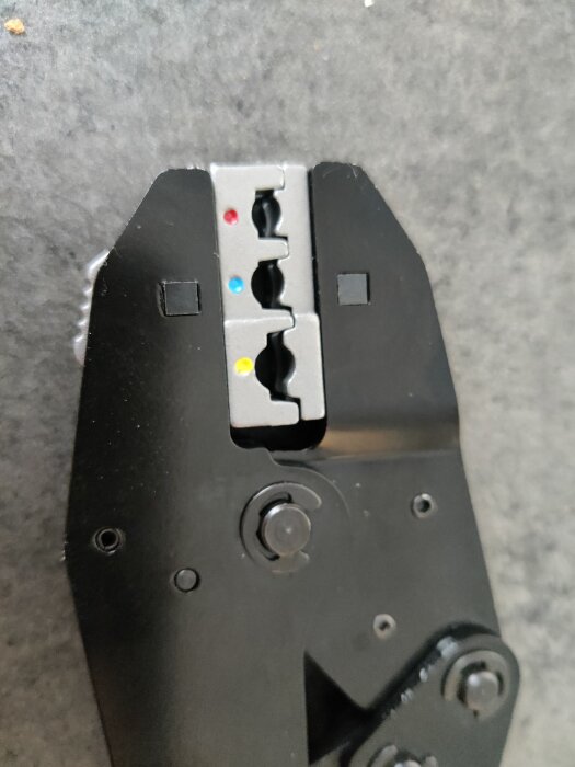 Tång för kabelskarvning, visar pressfäste med markeringar i röd, blå och gul färg mot en mörk bakgrund.