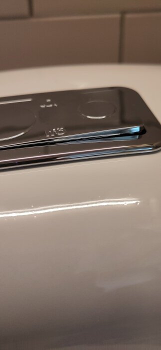 Närbild av spolknappen på ett Ifö 6262-toalettlock där knappen för låg volym tycks fastna och är något upphöjd.