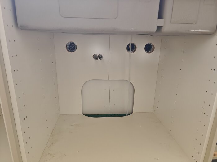 Tomt utrymme under diskbänk med synliga hål för rördragning.