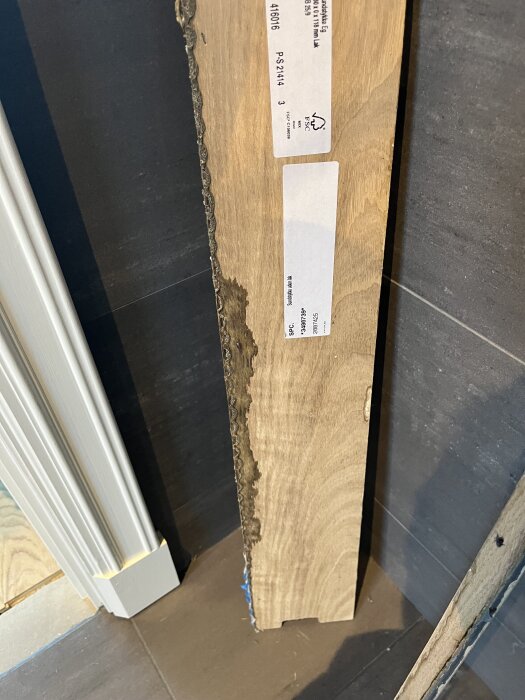 Bilden visar ett borttaget tröskelstycke med etiketter, stående mot en vägg.